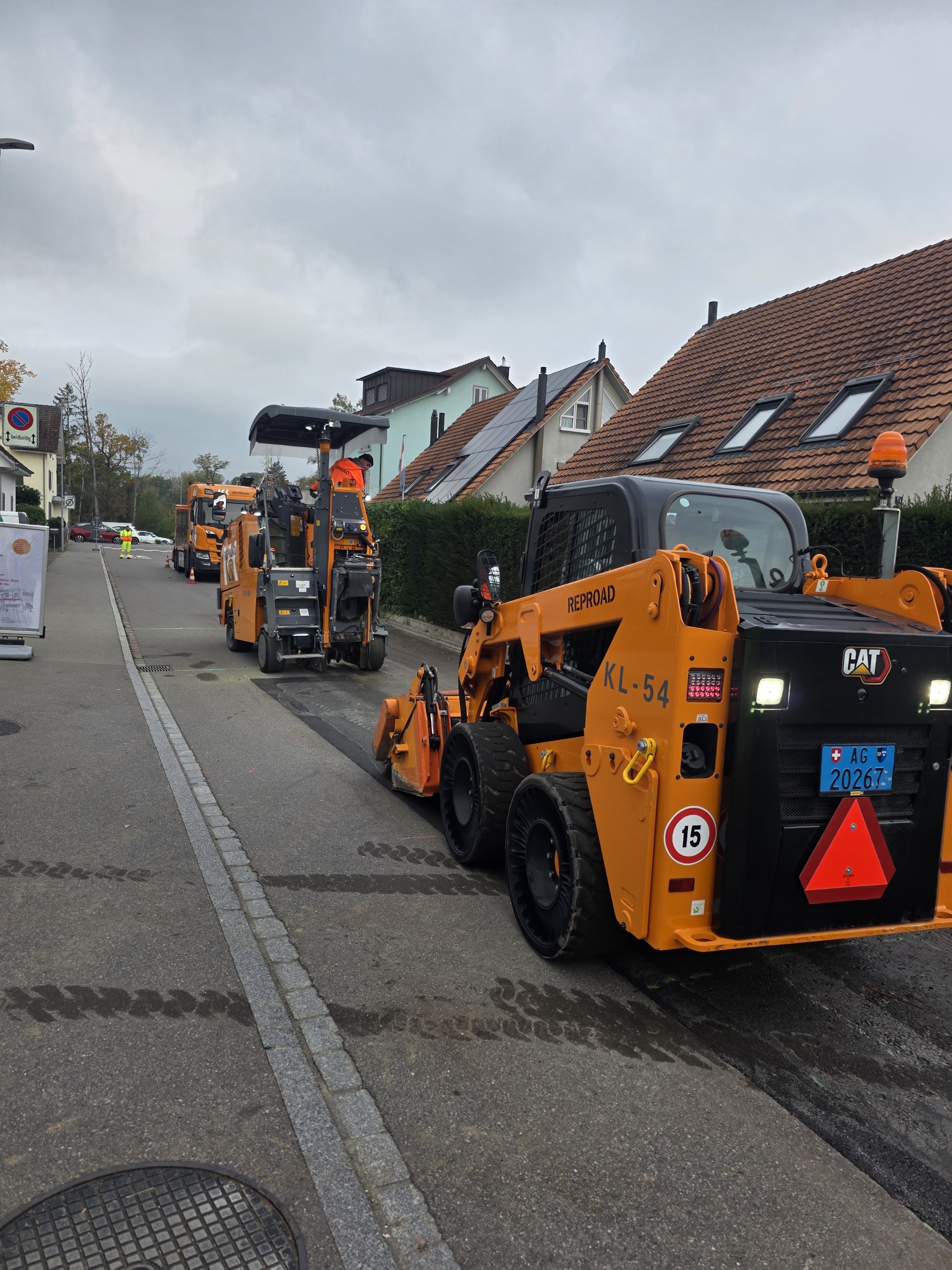 Kompaktlader auf einer Dorfstrasse mit Warndreieck